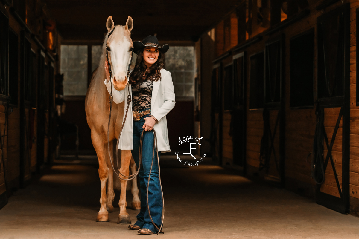 Amy with Palomino horse standing in barn aisle