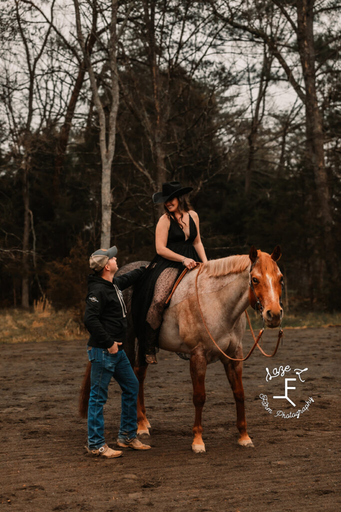 Amy in black dress on red roan with husband standing with her