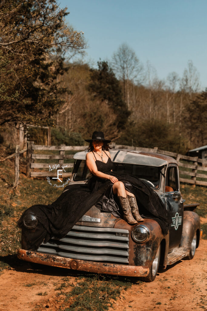 Gina in black dress sitting on hood of old truck
