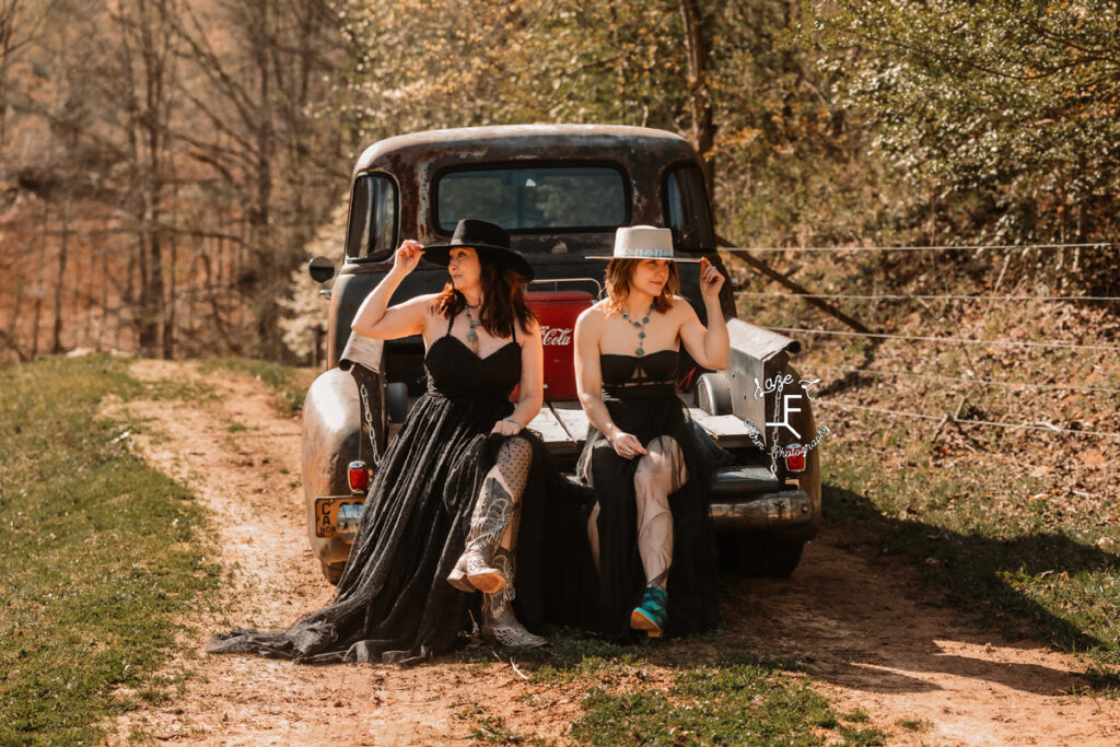 Gina and Christina in black dresses sitting on tailgate of old truck