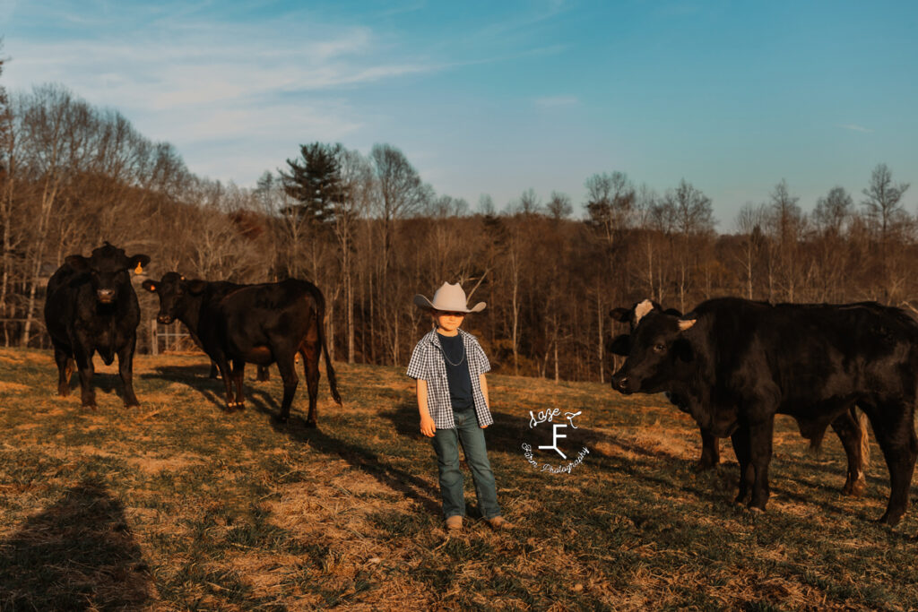 Cade with his cowboy hat on standing with cows