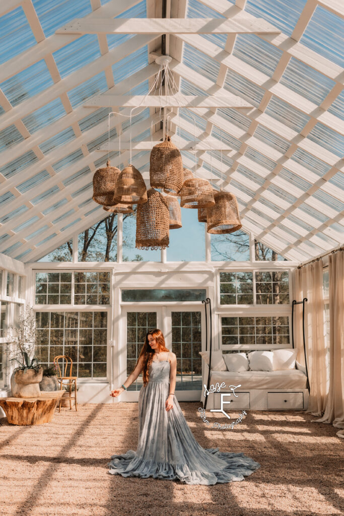 Bella in blue lace dress standing in middle of greenhouse