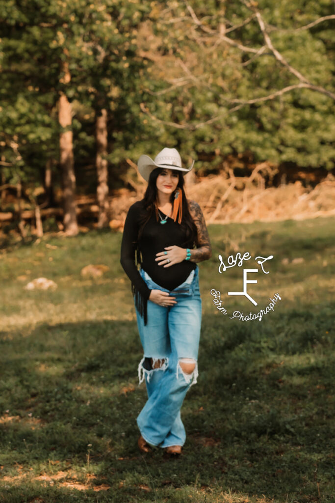 Kirstan in black shirt and jeans with white cowboy hat holding bump