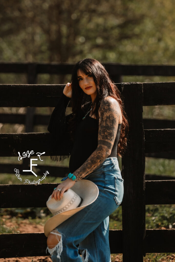 Kirstan leaned against fence holding cowboy hat