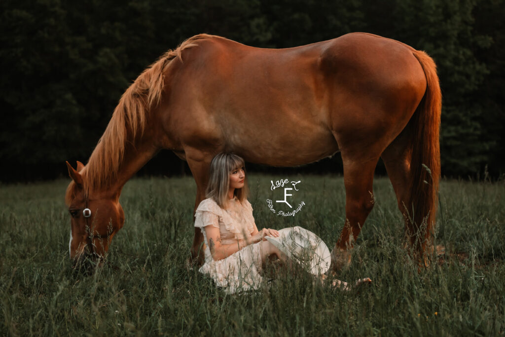 cowgirl sitting in the grass in front of her horse