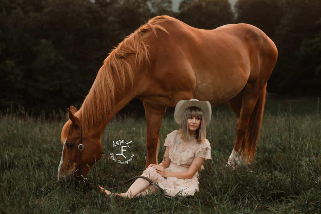 cowgirl sitting in the grass in front of her horse