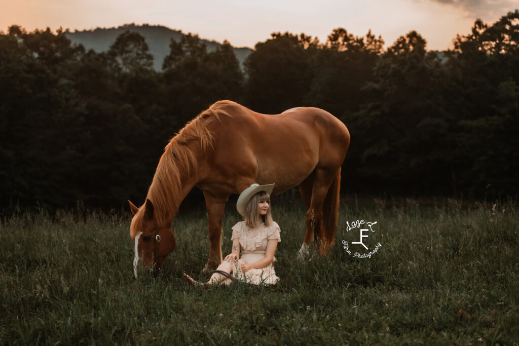 cowgirl sitting in the grass in front of her horse