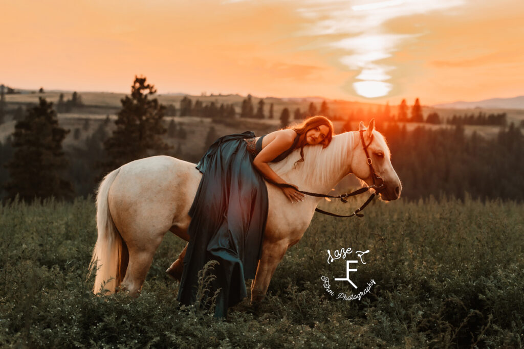 Tevis laying on Palomino horse at sunset