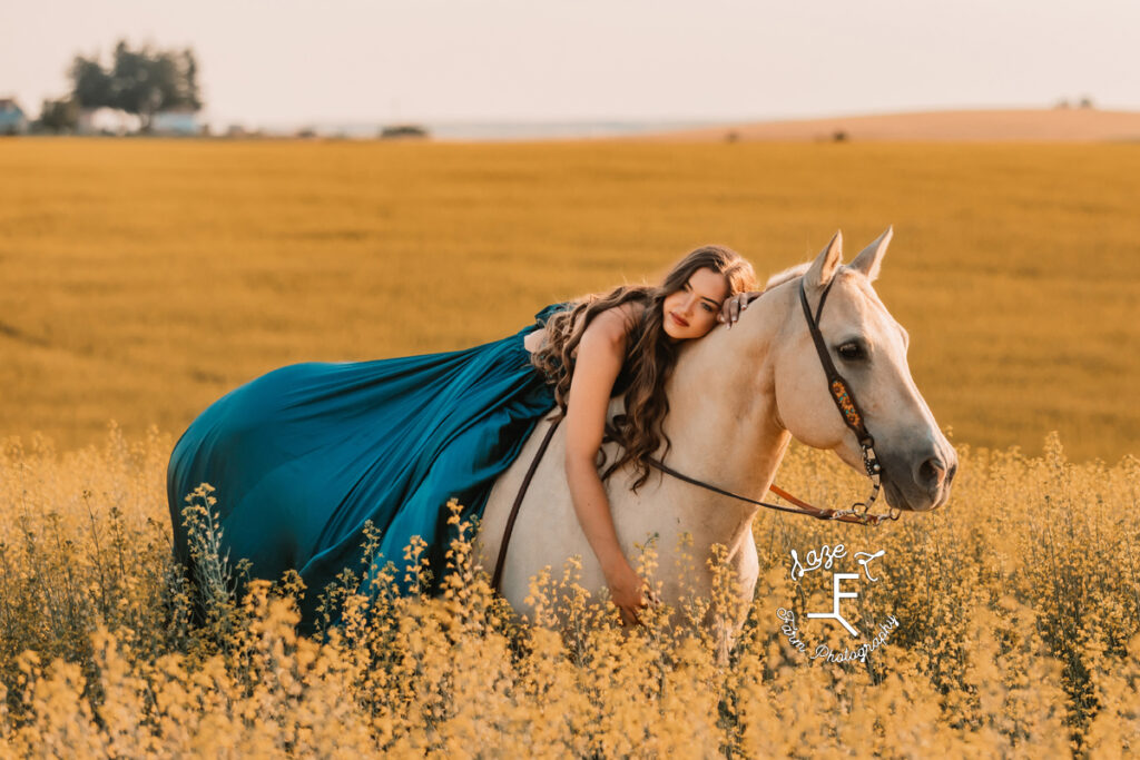 Tevis wearing blue dress laying on Palomino horse in a field