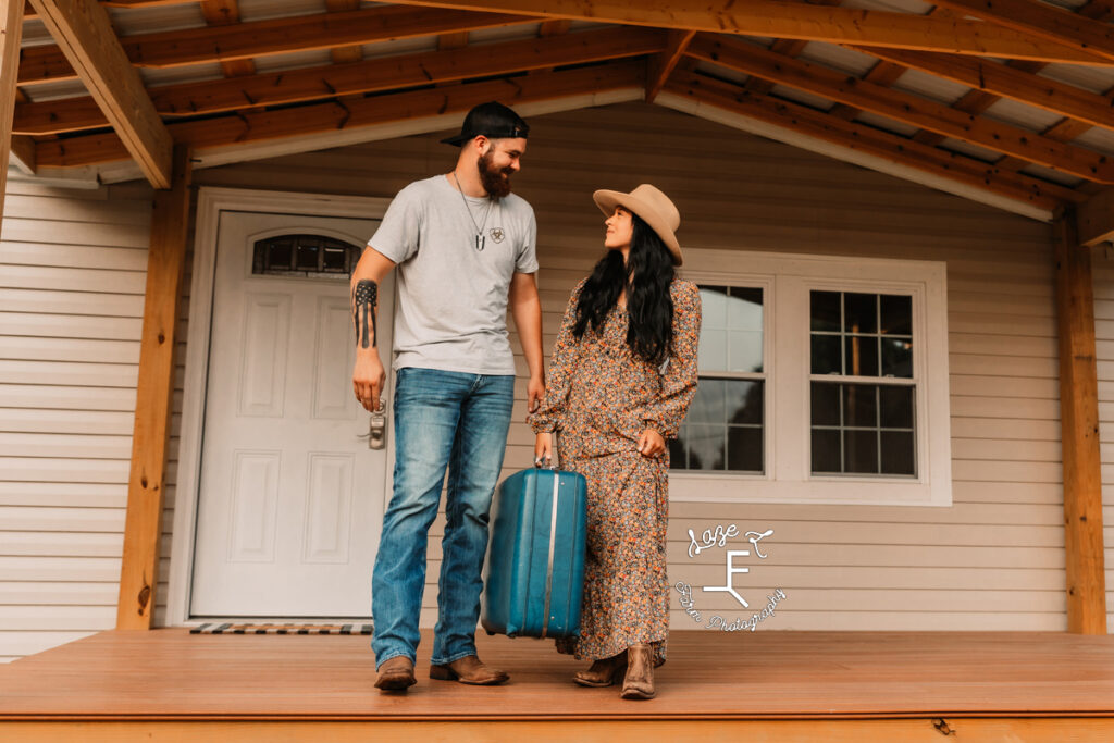 couple holding old suitcase on new porch to their house