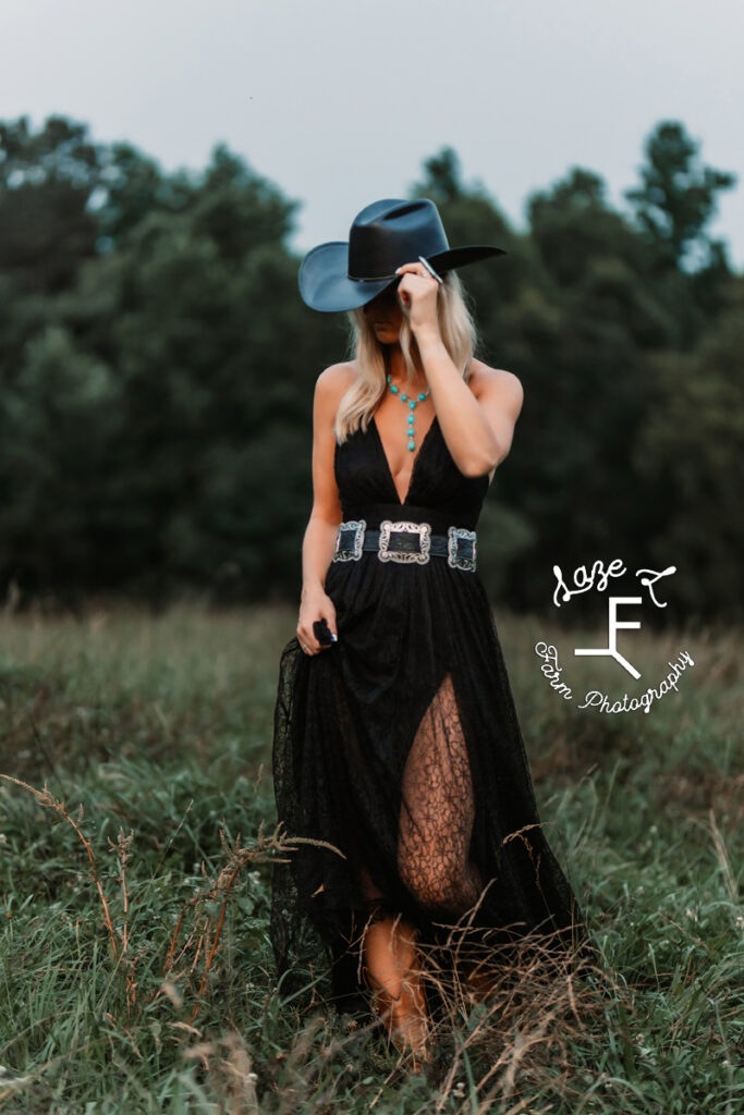 Model in black dress and hat touching hat looking down