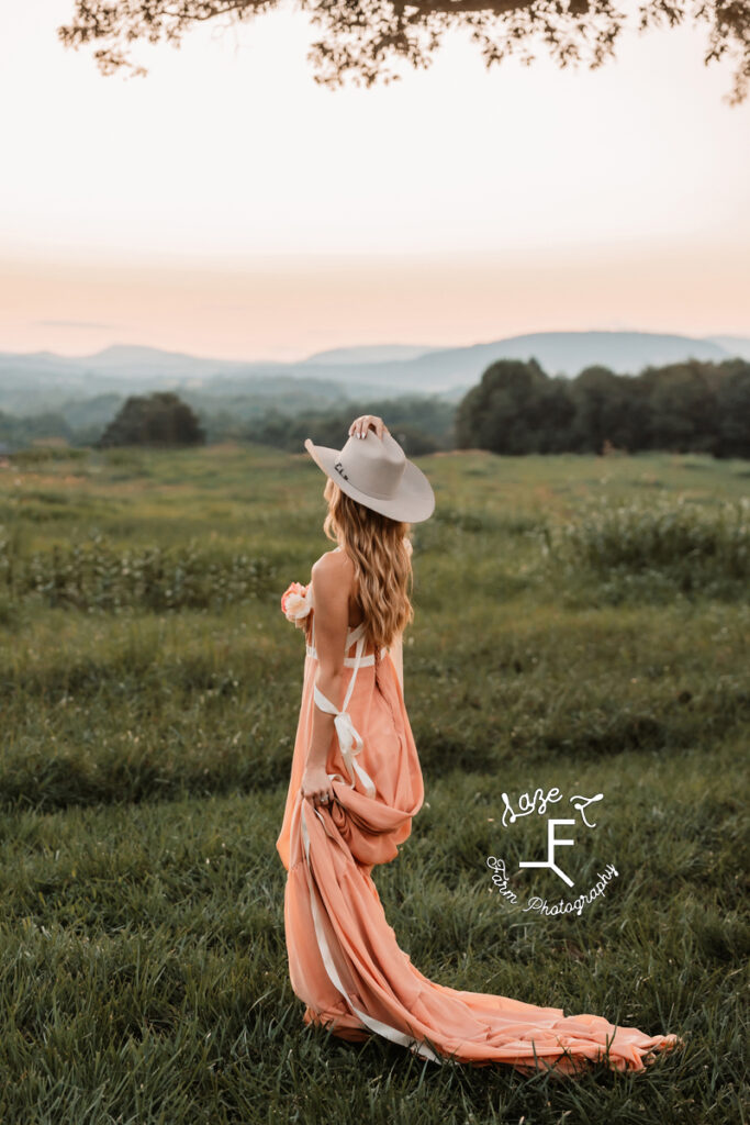 Payton in pink dress and cowboy hat facing away from camera at sunset