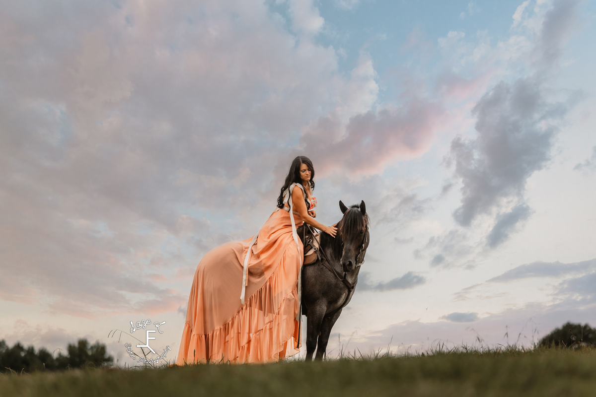 Danielle sitting on Chex on top of a hill at sunset petting him