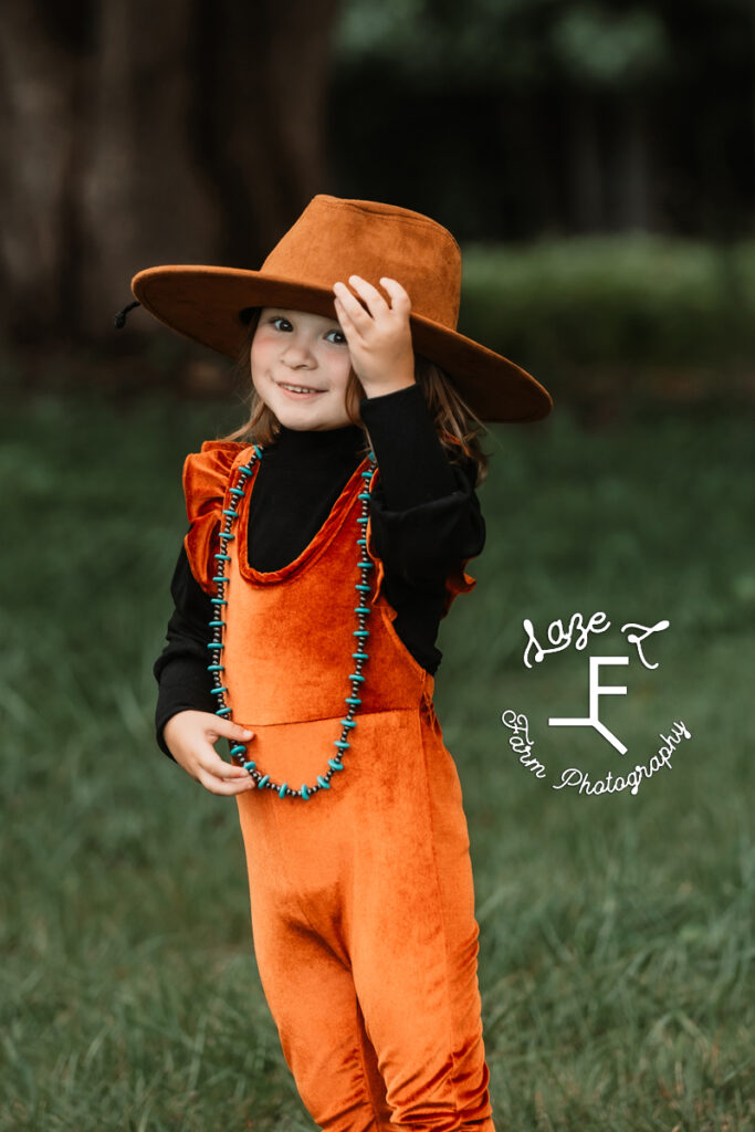 Lyza wearing a brown hat, orange jumpsuit and turquoise necklace