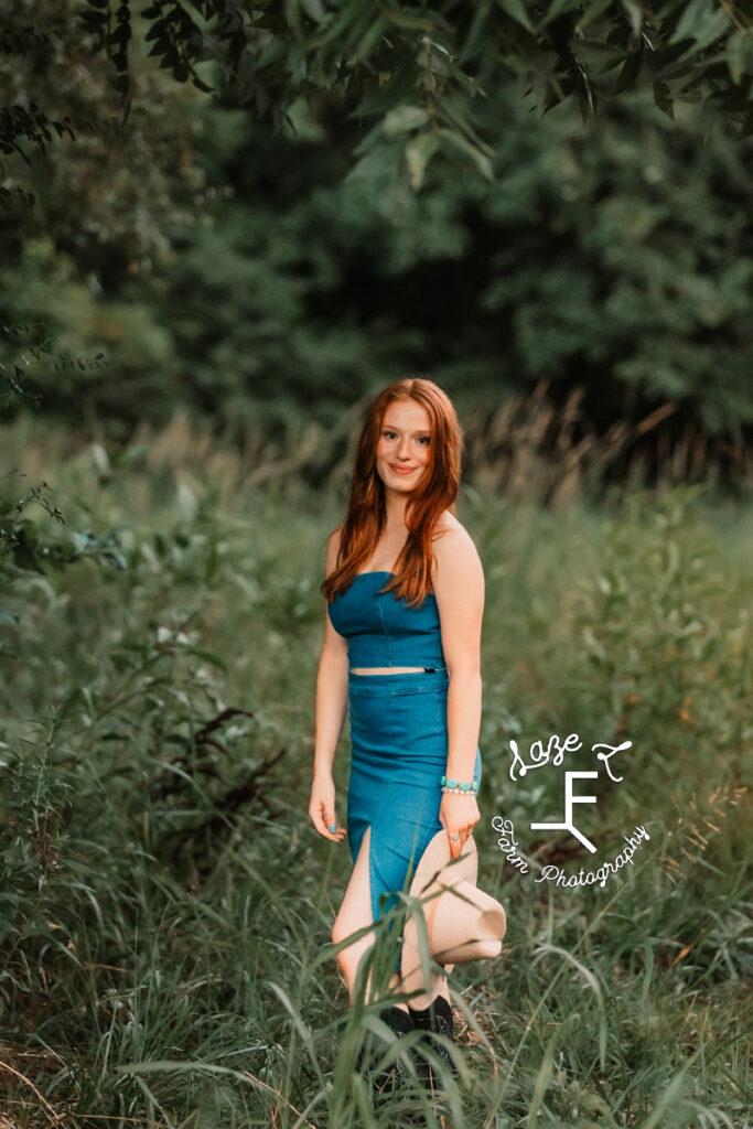 Kendall in blue jean dress outfit with hat standing in field