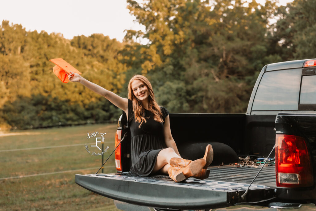 Kendall sitting on truck tailgate holding graduation cap