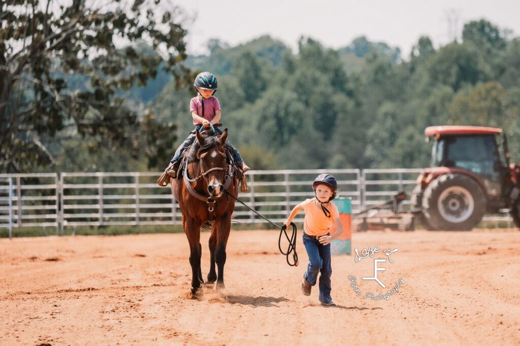 little girl leading another little girl on horseback