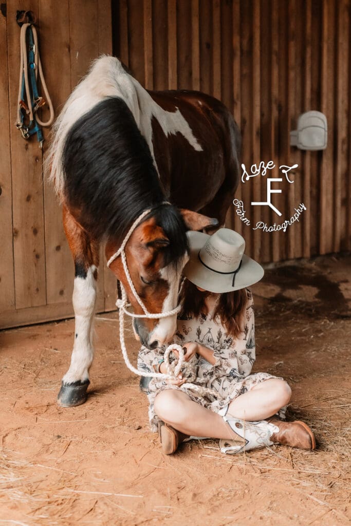 Natalie sitting on ground and paint pony putting his head to her