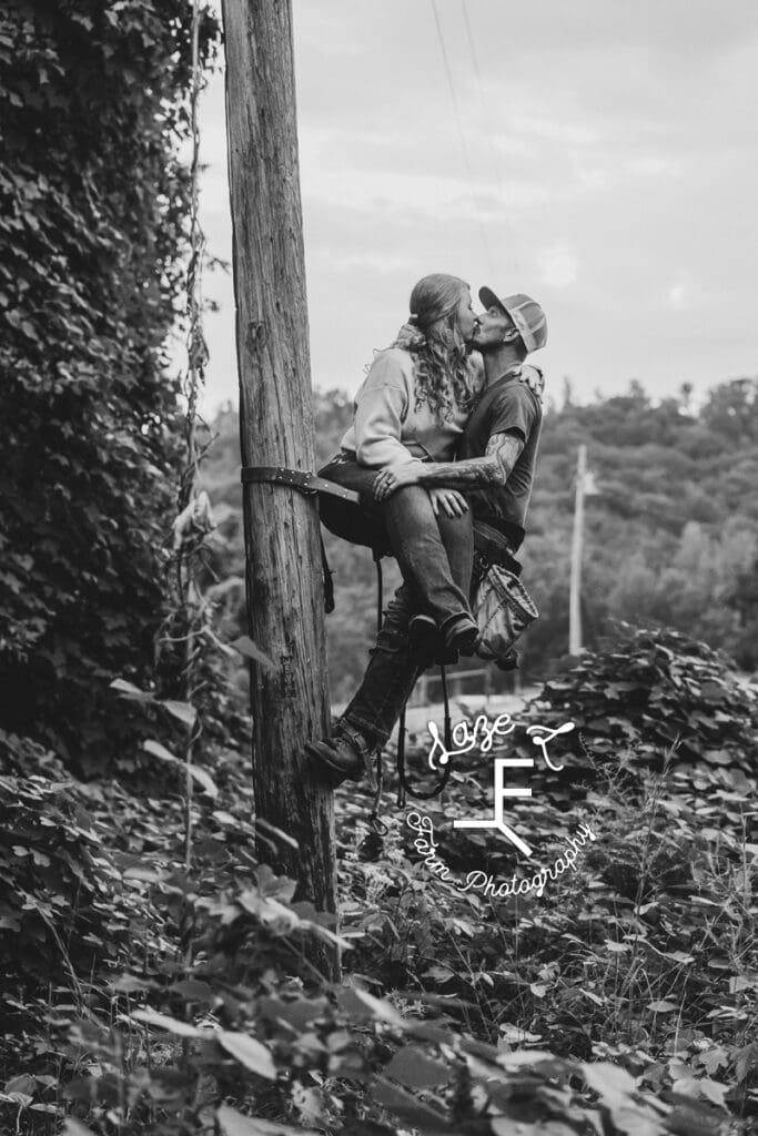 Kyle in his lineman gear on pole supporting taylor while they kiss