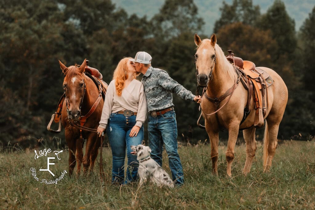 Taylor and Kyle standing with horses and dog kissing