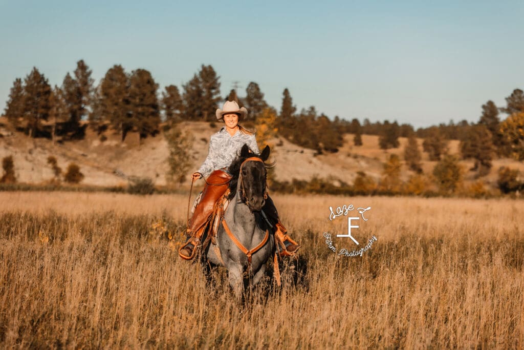 Cowgirl 2 riding roan horse in brown grass