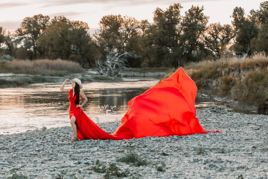 Cowgirl in red parachute dress touching hat by river