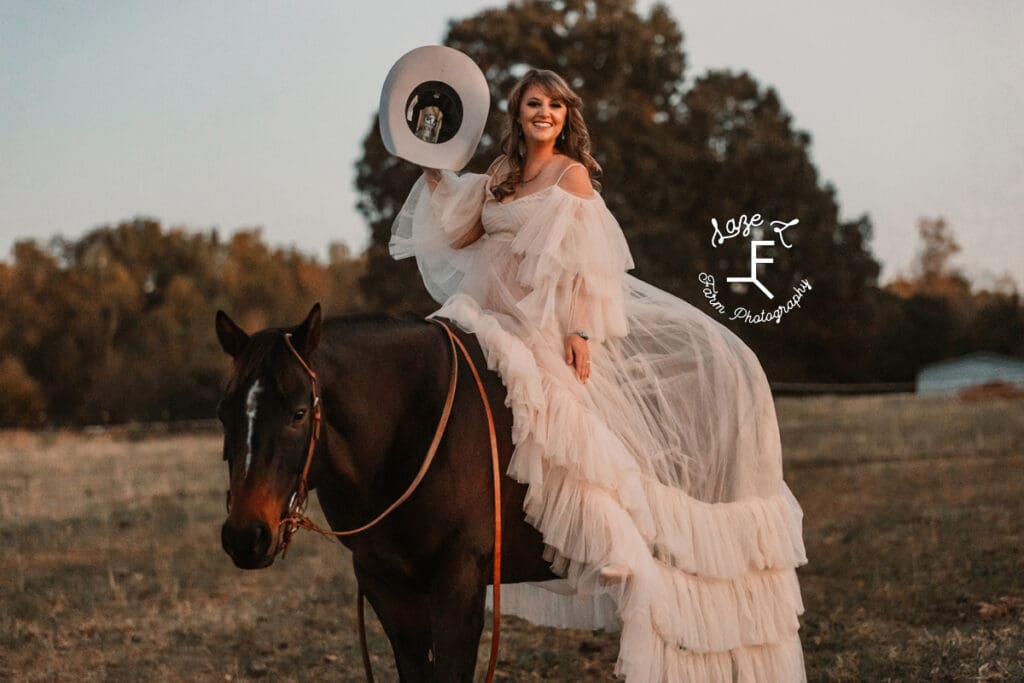 cowgirl on horseback in flowy dress holding hat