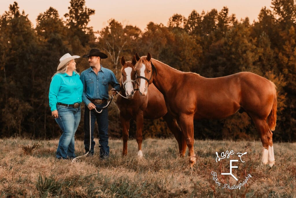 husband and wife standing looking at each other with 2 horses