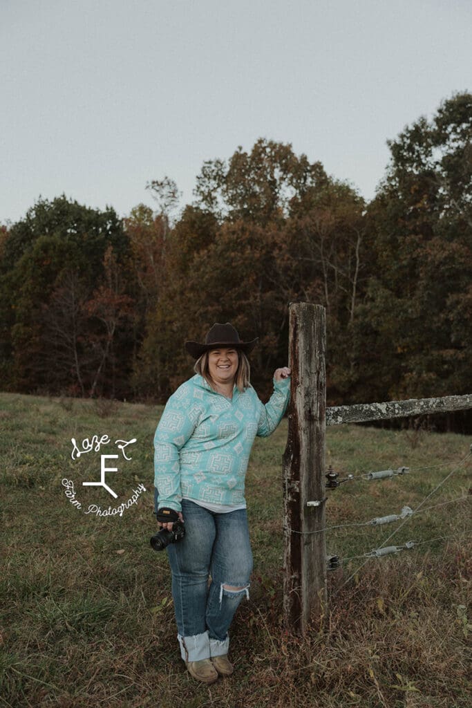 Sarah holding camera leaning on fence post