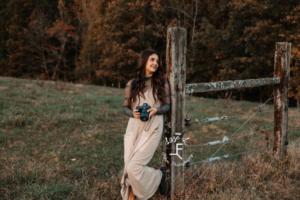 Gwen holding camera leaning on fence looking left