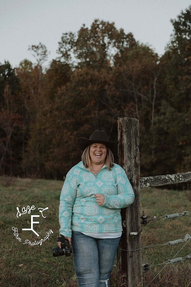 Sarah holding camera laughing in front of fence post