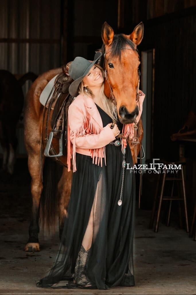 cowgirl standing with horse in the barn aisle