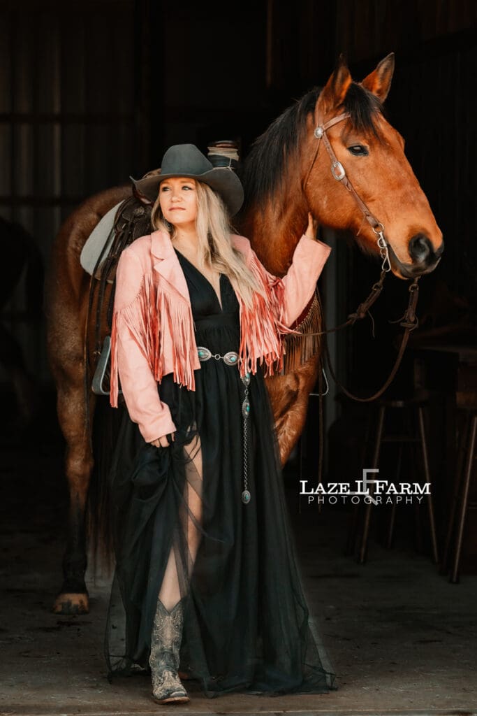 cowgirl standing with horse in the barn aisle
