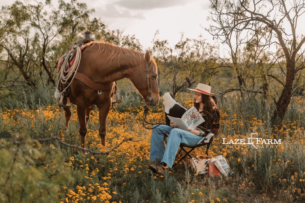 cowgirl reading a book in a flower field with her horse