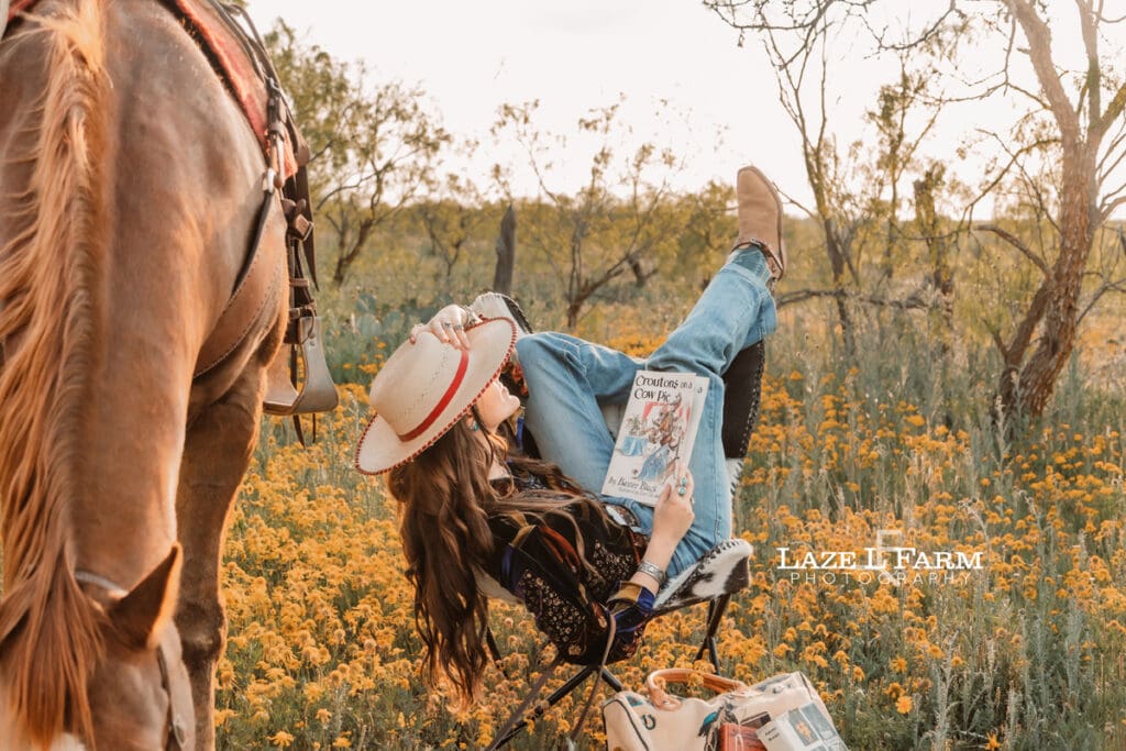 cowgirl reading a book in a flower field with her horse
