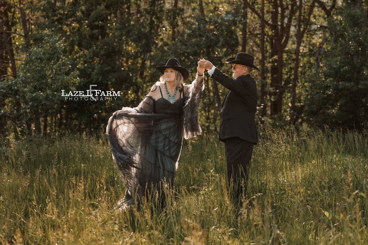couple standing in a field with flowers with the mountains behind them at sunset