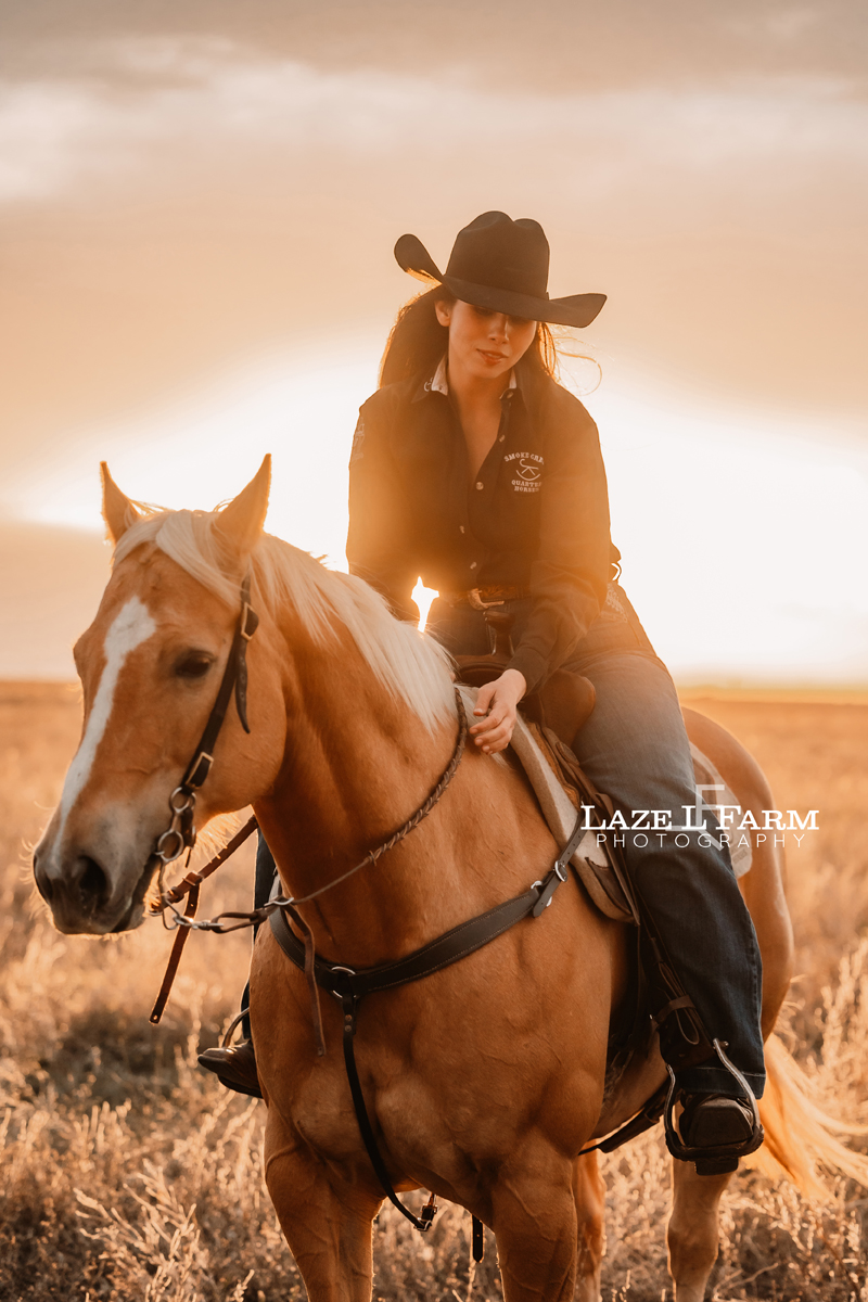cowgirl riding her palomino horse in an open field at sunset