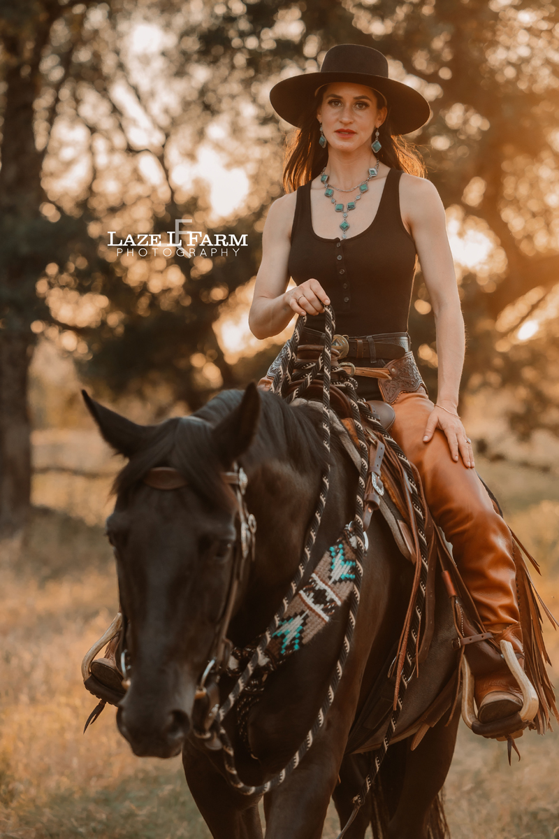 cowgirl riding her horse through a field at sunset
