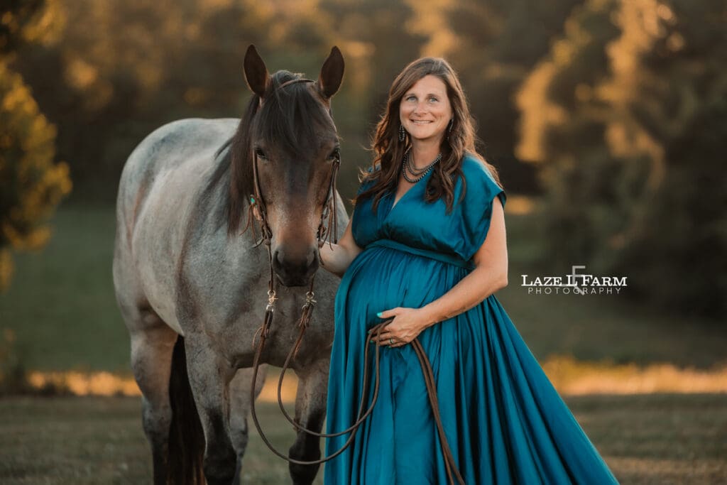 A girl standing beside her horse in a turquoise parachute dress during her maternity session with Laze L Farm Photography