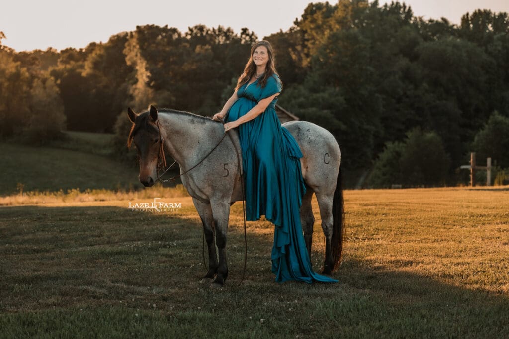 A girl standing beside her horse in a turquoise parachute dress during her maternity session with Laze L Farm Photography