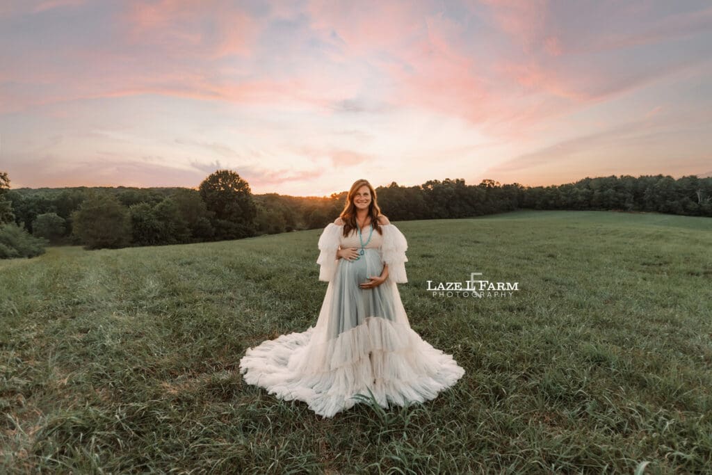 A girl standing in a middle of the field at sunset during her maternity session in a white dress during a photoshoot with Laze L Farm Photography