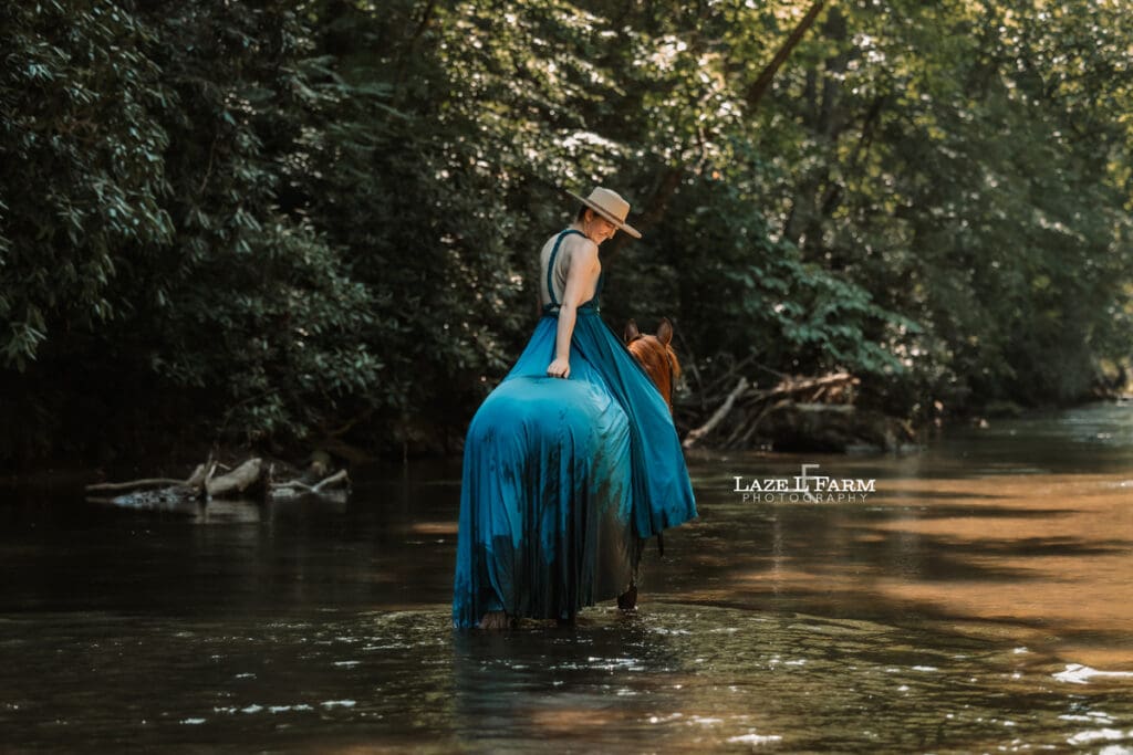 Cowgirl riding her horse in the creek wearing a turquoise parachute dress during a photoshoot with Laze L Farm Photography