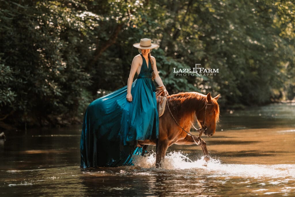 Cowgirl riding her horse in the creek wearing a turquoise parachute dress during a photoshoot with Laze L Farm Photography