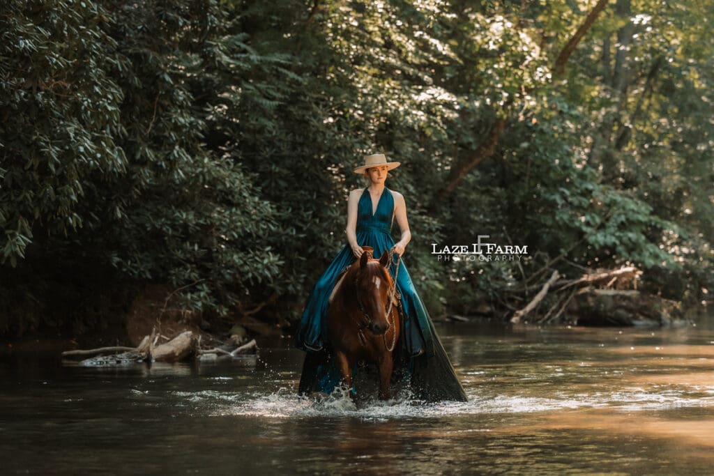 Cowgirl riding her horse in the creek wearing a turquoise parachute dress during a photoshoot with Laze L Farm Photography