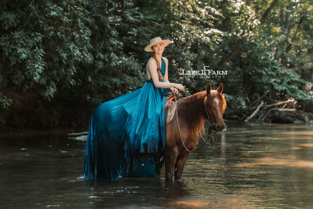 Cowgirl riding her horse in the creek wearing a turquoise parachute dress during a photoshoot with Laze L Farm Photography