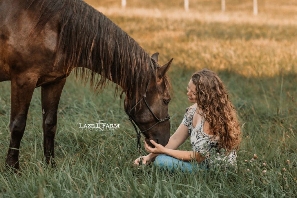 A girl sitting in a field with her horse during a photoshoot with Laze L Farm Photography