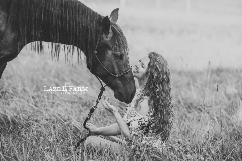 A girl sitting in a field with her horse during a photoshoot with Laze L Farm Photography